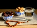 Cups with a traditional oriental pattern with dates and walnuts, a glass of clear water, stone rosary on a napkin during sunset