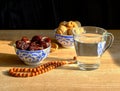 Cups with a traditional oriental pattern with dates and walnuts, a glass of clear water, stone rosary on the table during sunset