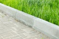 A curbstone separates the pedestrian zone from the green tall grass of the lawn. City improvement Royalty Free Stock Photo