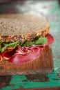 Cured meat sandwich with seeded bread on old wooden table