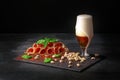 Cured prosciutto or balyk with pistachios, a spinach and a light beer with foam on a black background. Copy space. Pistachios and
