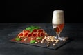 Cured prosciutto or balyk with pistachios, a spinach and a light beer with foam on a black background. Copy space. Pistachios and