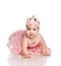 Curious little infant baby girl toddler in pink dress, crown on head is creeping on floor interested in camera