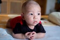 Curious Asian infant baby boy lie on the stomach or prone, wearing black red clothes on the bed