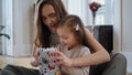 Curious baby opening gift at New Year house. Mom presenting toy to daughter