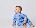 Curious barefooted blond baby boy toddler in blue fleece jumpsuit with stars sits on the floor, turn and going to crawl