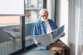 Curious bearded pensioner reading newspaper on windowsill Royalty Free Stock Photo