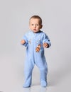 Blond baby boy toddler in blue cotton jumpsuit with rainbow and tiger walks holding hands up