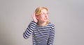 Curious blond young woman with hand near ear trying to overhead while standing on white background Royalty Free Stock Photo