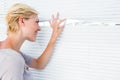 Curious blonde woman looking through venetian blind