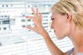 Curious blonde woman looking through venetian blind