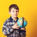 Curious boy holding earth globe map. Little traveler, isolated on yellow. Kid exploring the new horizons at globe. Funny kid with