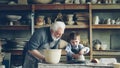 Curious boy is learning pottery from his experienced grandfather in small home studio. Child is forming clay to make Royalty Free Stock Photo