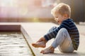 A curious child, a boy, barefoot touches the water of a city fountain. Hot and sunny summer day, the water is a good refreshment Royalty Free Stock Photo