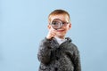Curious creepy little ginger boy in glasses looking through the magnifying glass