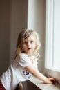 Curious cute little girl standing on a chair at the window, blonde curls