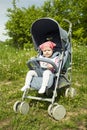 Curious European girl in a pink scarf in a blue stroller for a walk. Baby girl 9 months carefully. Focused smart look, small child