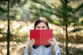 Curious eyes peek over a red book held by a person in a light blue shirt, creating a playful