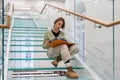 Curious female reader sits on modern glass stairs step reading favorite book about world history
