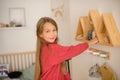 Girl with long hair in pink sweater in children`s room of  youngest child in family, climbed to wall shelves with toys and Royalty Free Stock Photo