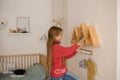 Girl with long hair in pink sweater in children`s room of  youngest child in family, climbed to wall shelves with toys and Royalty Free Stock Photo