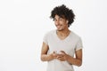 Curious good-looking male with afro haircut, tilting head and smiling joyfully, holding smartphone and wearing wireless Royalty Free Stock Photo
