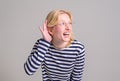 Curious happy blond young woman with hand near ear trying to listen gossip over white background Royalty Free Stock Photo