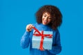 Curious and happy, smiling african-american woman, b-day girl in winter sweater, pulling present knot to unwrap gift and Royalty Free Stock Photo
