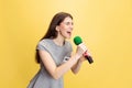 Emotional young girl, female reporter holding reporter microphone isolated on yellow studio background. Concept of