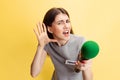 Emotional young girl, female press representative holding reporter microphone isolated on yellow studio background