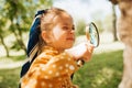 Curious kid with magnifying glass exploring the nature outdoor. Adorable little explorer girl playing in forest with magnifying