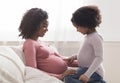 Curious little black girl touching her pregnant mother`s belly at home