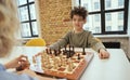 Curious little boy sitting in the classroom and watching his friend making a move while playing chess on the chessboard Royalty Free Stock Photo