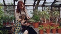 Curious little girl is helping her mom to spray plants with water from spraybottle while working together in orchard