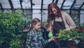 Curious little girl is helping her mom to spray plants with water from spraybottle while working together in orchard