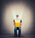 Curious man sitting on a chair in a dark room holding yellow box on knees, looking inside as a magic light come out of the bin Royalty Free Stock Photo