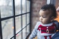 Curious mixed-race baby looking out of the window and developing cognitive functions.