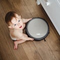 A curious oddler baby boy is playing with a robot vacuum cleaner on th Royalty Free Stock Photo