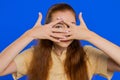 Curious redhead adult woman closing eyes with hand and spying through fingers, hiding and peeping Royalty Free Stock Photo