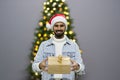 Curious Santa man sitting in front of Christmas tree background. Smiling handsome man with present after the opening in the gift Royalty Free Stock Photo