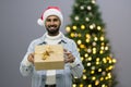 Curious Santa man sitting in front of Christmas tree background. Smiling handsome man with present after the opening in the gift Royalty Free Stock Photo