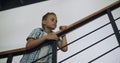 Curious schoolboy standing stairway alone. Boy leaning on railings examine hall.