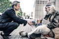 Curious short-haired businessman sitting in front of long-haired homeless