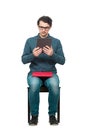 Curious student man seated on a chair using a PC tablet while holds a red book on his knees. Choose modern computer education