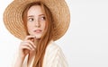 Curious thoughtful charming ginger girl with cute freckles in trendy summer straw hat turning right and gazing with