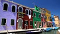 Curious tourists walking street on Burano island, photographing colored houses