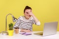 Curious woman sitting at workplace with laptop and spying, looking through fingers with interest.