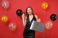 Curious young girl in black dress holding credit card, colored packages bags with purchases after shopping on bright red Royalty Free Stock Photo