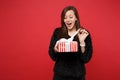 Curious young girl in fur sweater opening red striped present box with gift ribbon isolated on red background. Valentine Royalty Free Stock Photo