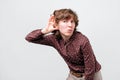 Woman with curly hair placing hand on her ear, listening attentively, trying to overhear